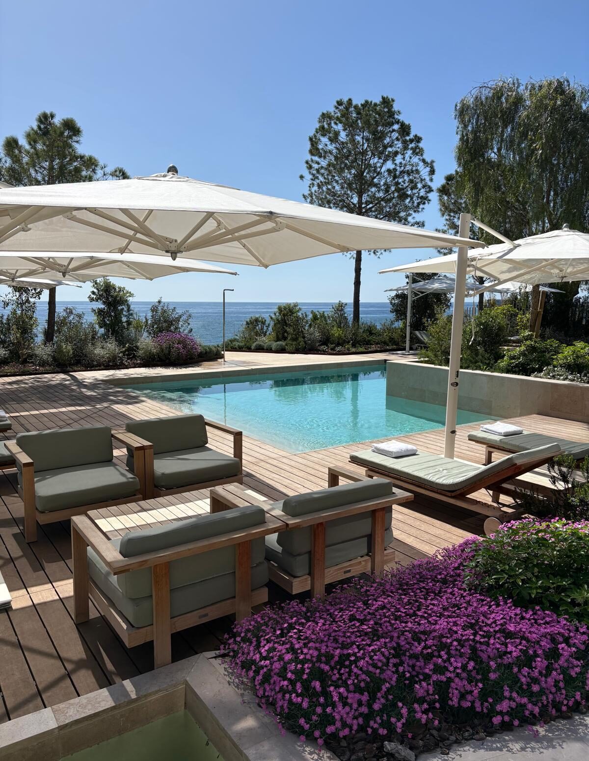 One of the pools in Les Jardins d'Eau on a sunny day. Patio with a pool and blooming flowers